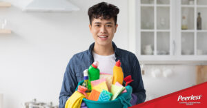 College student holding a bucket of cleaning supplies in a kitchen, promoting Peerless Cleaning & Restoration’s back-to-school cleaning checklist.